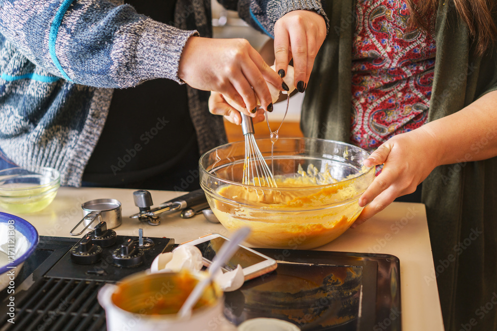 Fototapeta premium two sisters making pumpkin pie batter and cracking egg over bowl to be whisked in