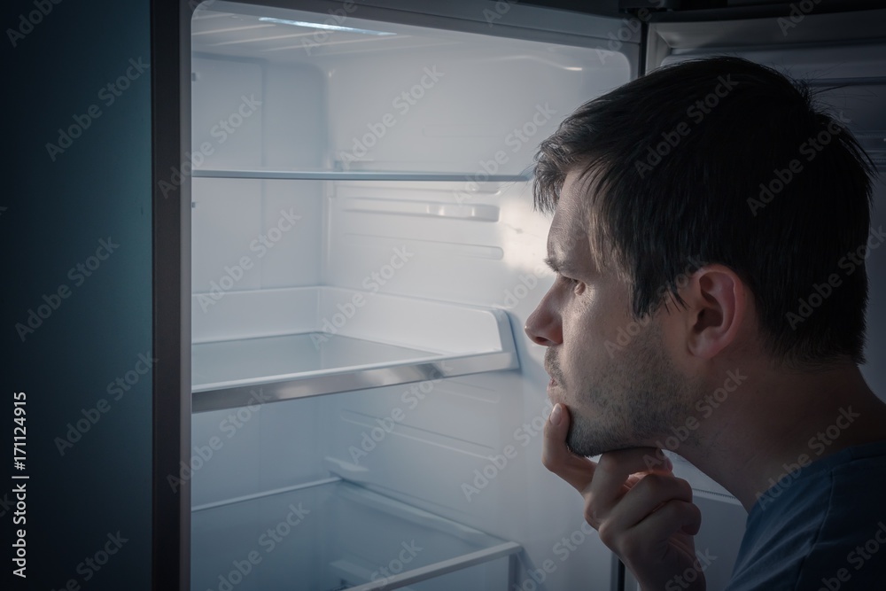Hungry man is looking for food to eat in empty fridge at night.