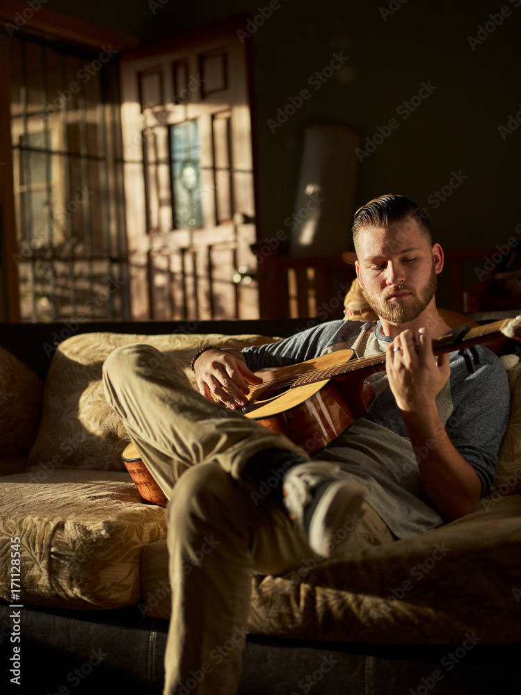 man playing guitar on sofa at home