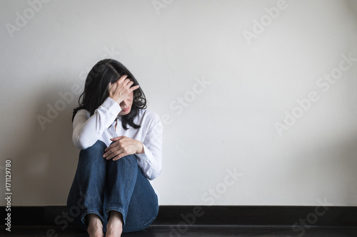 Stressful woman sitting sadly with emotional depression and anxiety on the floor in home living room with white wall