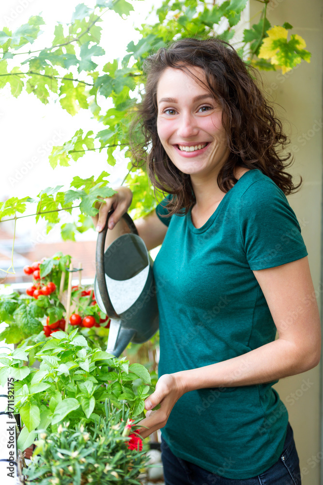 Young woman watering tomatoes on her city balcony garden - Nature and ecology theme Young woman watering tomatoes on her city balcony garden - Nature and ecology theme
