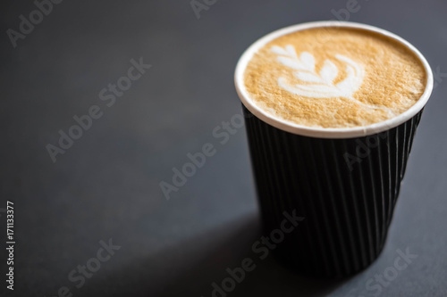 Soft focus of Latte art hot coffee in black paper cup on gray background with shadow , blurred and soft focus image