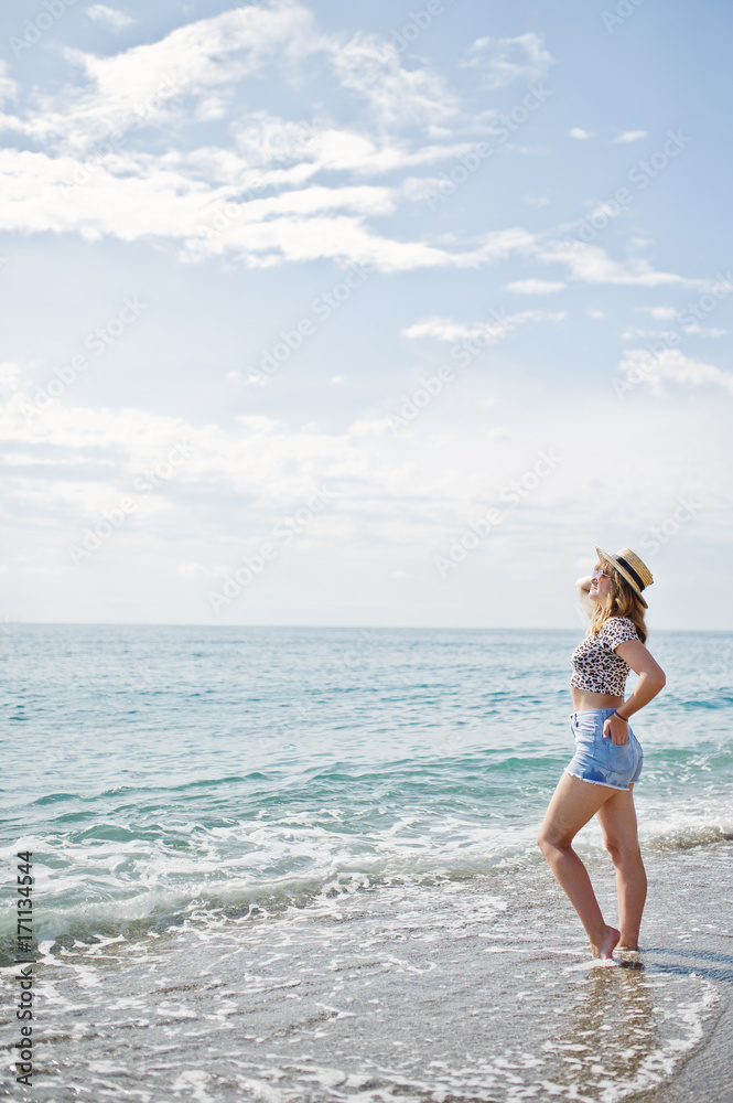Beautiful model relaxing on a beach of sea, wearing on jeans short, leopard shirt and hat.