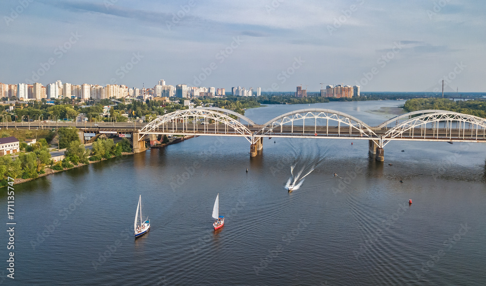 Aerial top view of Darnitsky bridge, yachts and boats sailing in Dnieper river from above, Kiev (Kyiv) city skyline, Ukraine

