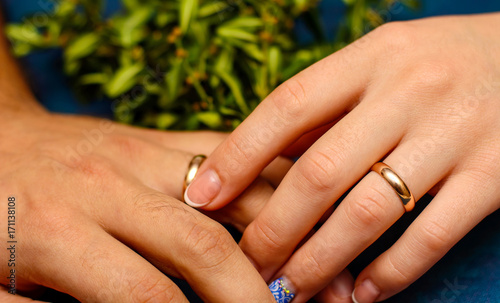 Photo of hands with beautiful wedding rings and green leaves on blue background