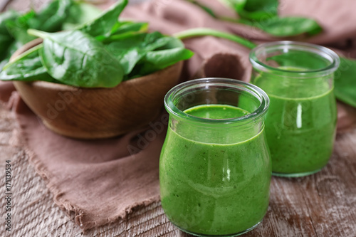 Jars of spinach smoothie on wooden table