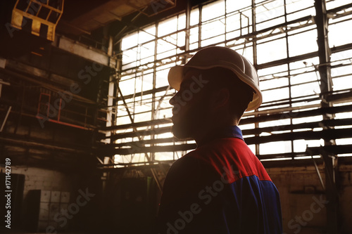 Silhouette of a worker in a construction helmet against a background of a factory or production