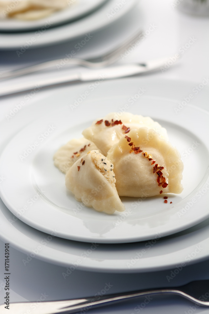 Elegant russian dumplings with red pepper lay on white tableware in luxury restaurant.
