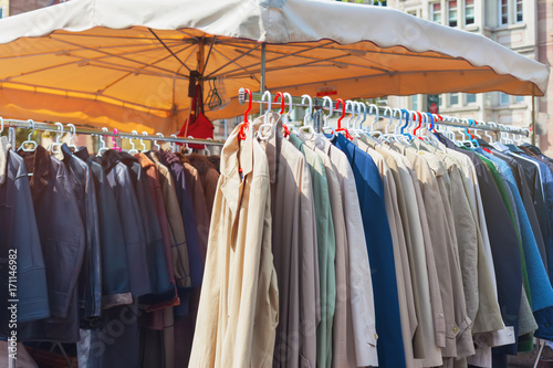 Clothes for sale hanging on a rack at outdoor flea market. © tiana__lima__