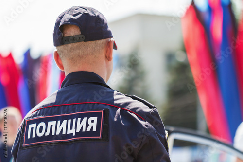 Policeman standing back to camera with inscription in russian Police on the uniform jacket. Protection of public order during city celebrations