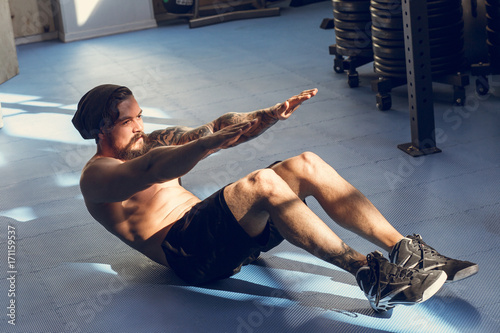 Handsome muscular man doing sit-ups on gym floor photo