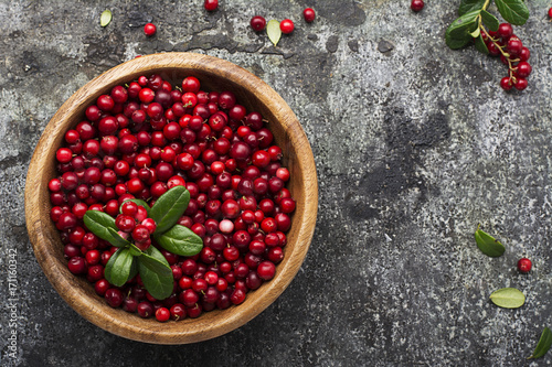 Red lingonberry in wooden bowl on rustic surface, top view photo