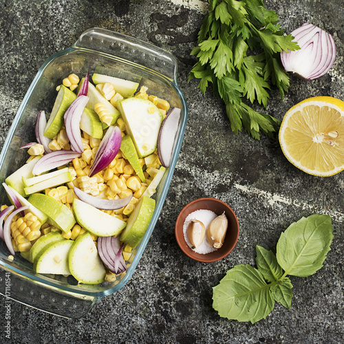 Top view of a vegetable casserole, kasserol of fresh seasonal vegetables cauliflower, corn, zucchini, red onion in a transparent form for baking for lunch.. photo