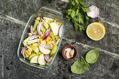 Top view of a vegetable casserole, kasserol of fresh seasonal vegetables cauliflower, corn, zucchini, red onion in a transparent form for baking for lunch.. photo