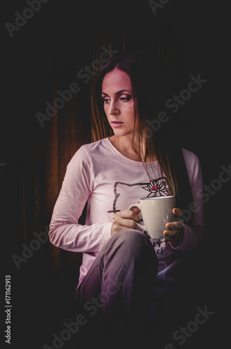 Obraz na płótnie Beautiful young woman drinking coffee and looking through window while sitting at windowsill at home w salonie