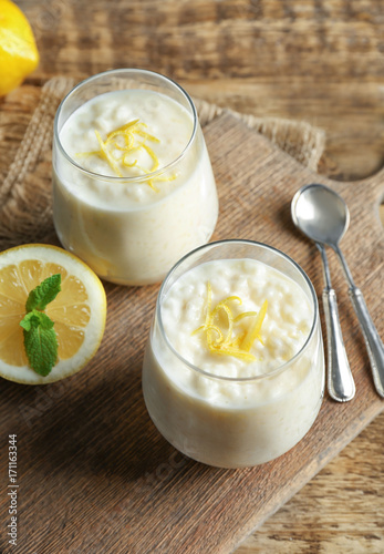 Creamy rice pudding with lemon in glasses on wooden table