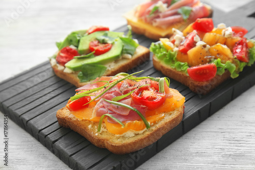 Wooden board with tasty sandwiches on table