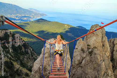 Woman is walking along a suspension bridge over an abyss.