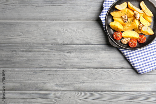 Frying pan with delicious baked potato wedges on wooden background