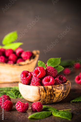 Fresh raspberries in wooden bowl on white table.