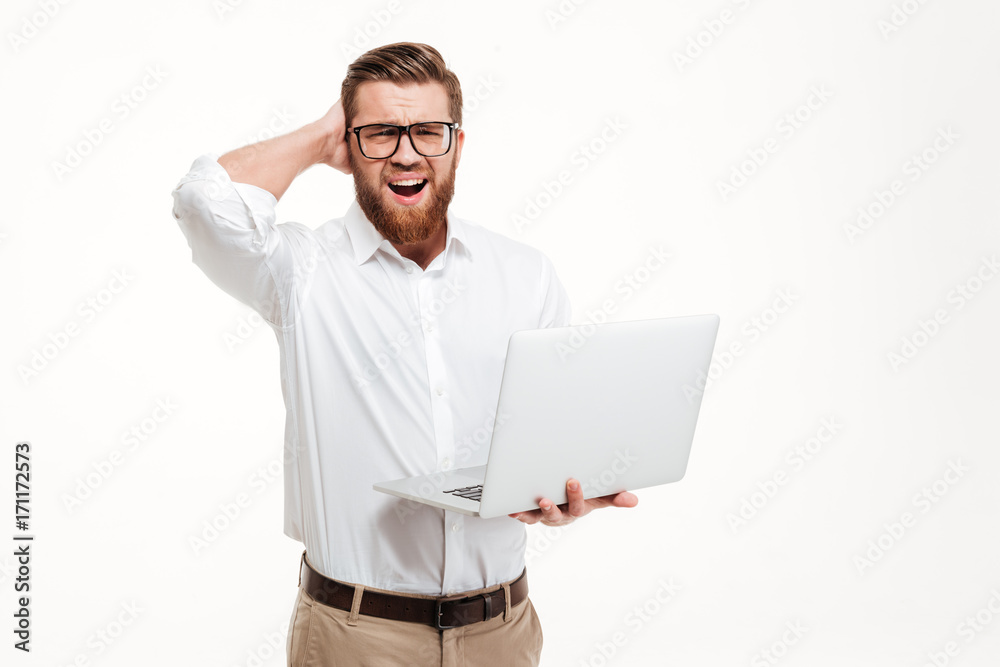 Confused bearded man holding laptop computer and scratching his head Confused bearded man holding laptop computer and scratching his head