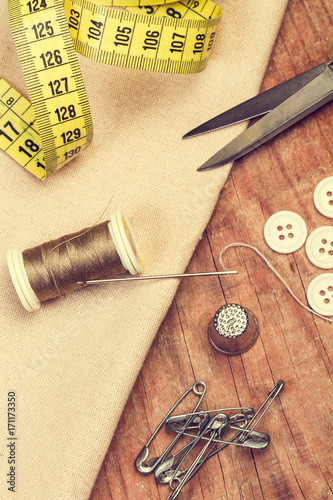 Hilo de coser, tela, cinta métrica, alfileres , botones, dedal y tijera sobre una mesa de madera. Vista superior. Concepto: Costura