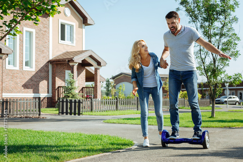 Caring wife holding hand of husband riding hoverboard