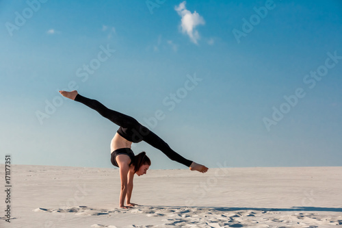 Fototapet Young woman practicing handstand on beach with white sand and bright blue sky
