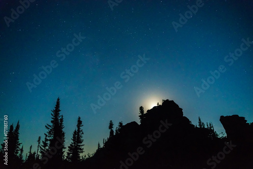 Stars and the moon against the backdrop of silhouettes of trees and rocks  