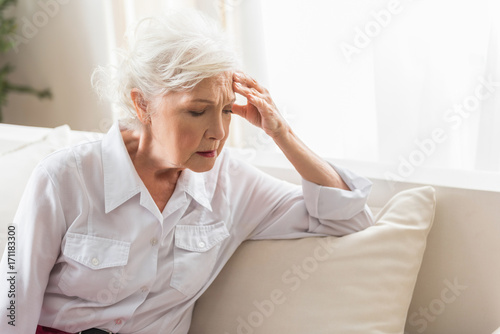 Aged female is sitting on sofa and feeling pain