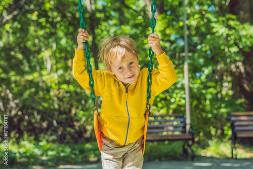 A boy in a yellow sweatshirt sits on a swing on a playground in autumn photo