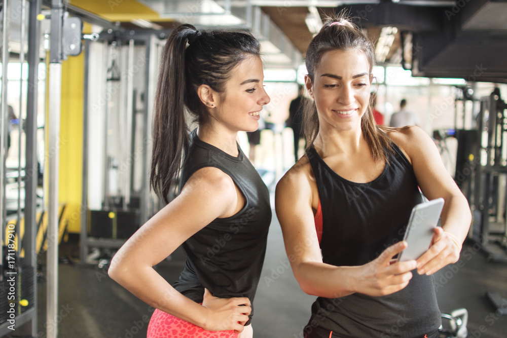 Two sporty girls looking something on mobile phone in gym.