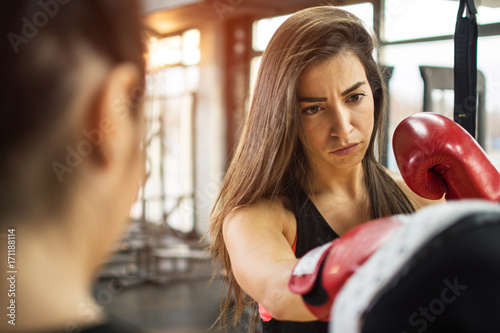 Beautiful brunette girl with red gloves exercising kick boxing at gym.