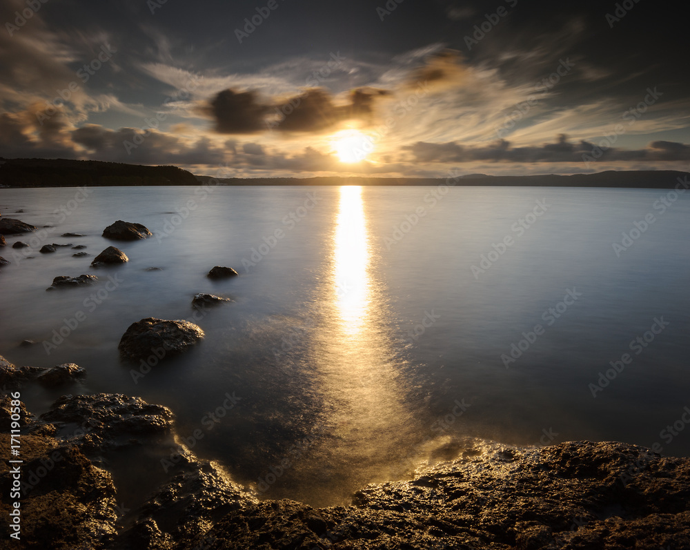 Big Torch: harsh bath of light for the rocks on the shore before the golden hours. Lake di Bracciano, Province of Rome, Lazio, Italy, Europe. Big Torch: harsh bath of light for the rocks on the shore before the golden hours. Lake di Bracciano, Province of Rome, Lazio, Italy, Europe.