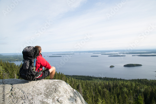 Hiker sits on the summit Paha-Koli and enjoys the scenery of the Pielinen lake, summer photo