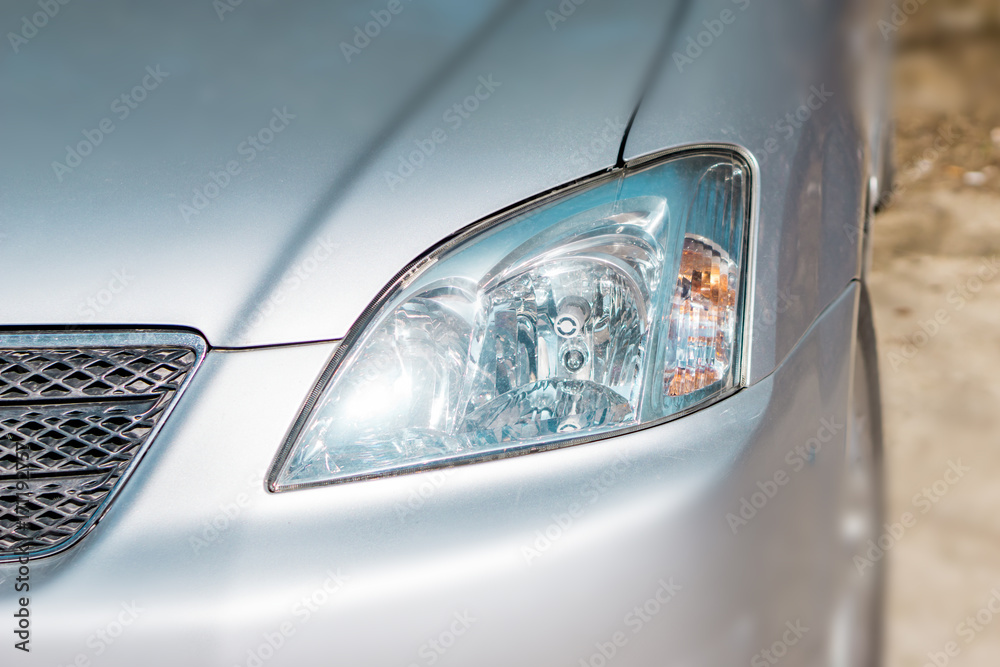 Headlight of a gray metallic car with reflection. Shallow depth of focus.