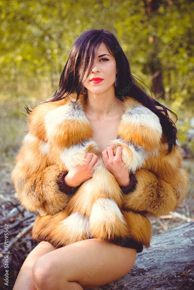 Young woman in luxurious furs with a naked body in the forest against a background of nature. Beautiful lady posing near trees in a fur coat Young woman in luxurious furs with a naked body in the forest against a background of nature. Beautiful lady posing near trees in a fur coat
