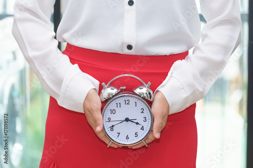 Woman holding alarm clock with red skirt - woman on her period. photo