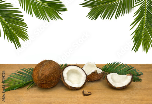 Coconut (Cocos nucifera) with half and palm leaves on wooden table on a white background.