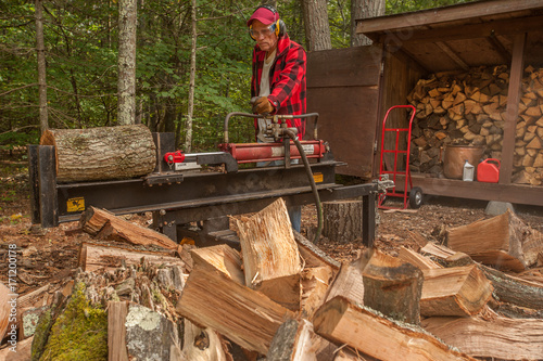Older man using log splitter near a wood shed