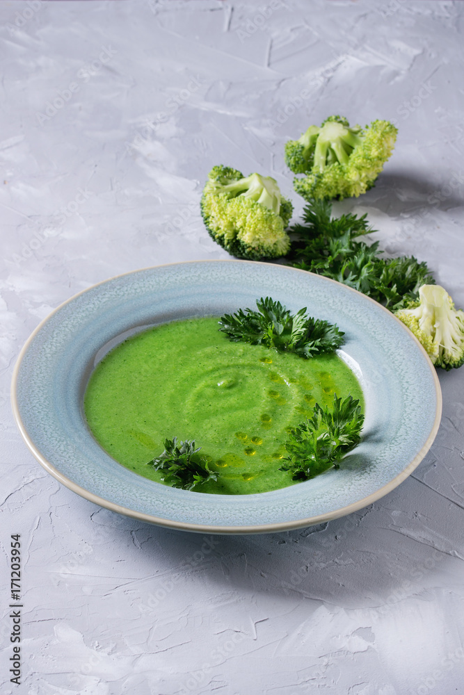 Vegetarian vegan broccoli cream soup served in blue plate with fresh parsley and broccoli over gray concrete background. Copy space. Healthy eating. Vegetarian vegan broccoli cream soup served in blue plate with fresh parsley and broccoli over gray concrete background. Copy space. Healthy eating.