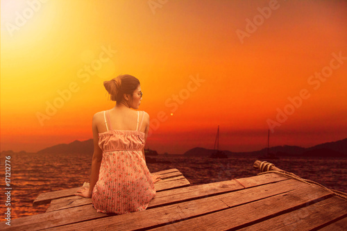Young woman sitting on wood pier looking in the sunset view.