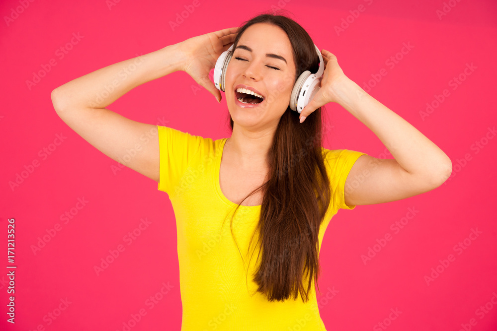 Beautiful young woman in black and yellow vibrant dress dances as she listens to the music over pink background Beautiful young woman in black and yellow vibrant dress dances as she listens to the music over pink background