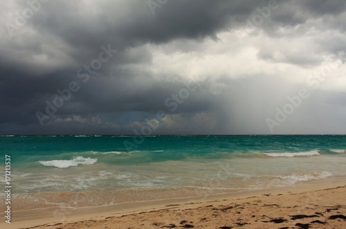 Rainy tropical storm coming from the atlantic ocean to the caribbean shore. Gloomy dark cloudy sky, turbulent sea waves. Empty overcast beach just before the wild rainfall