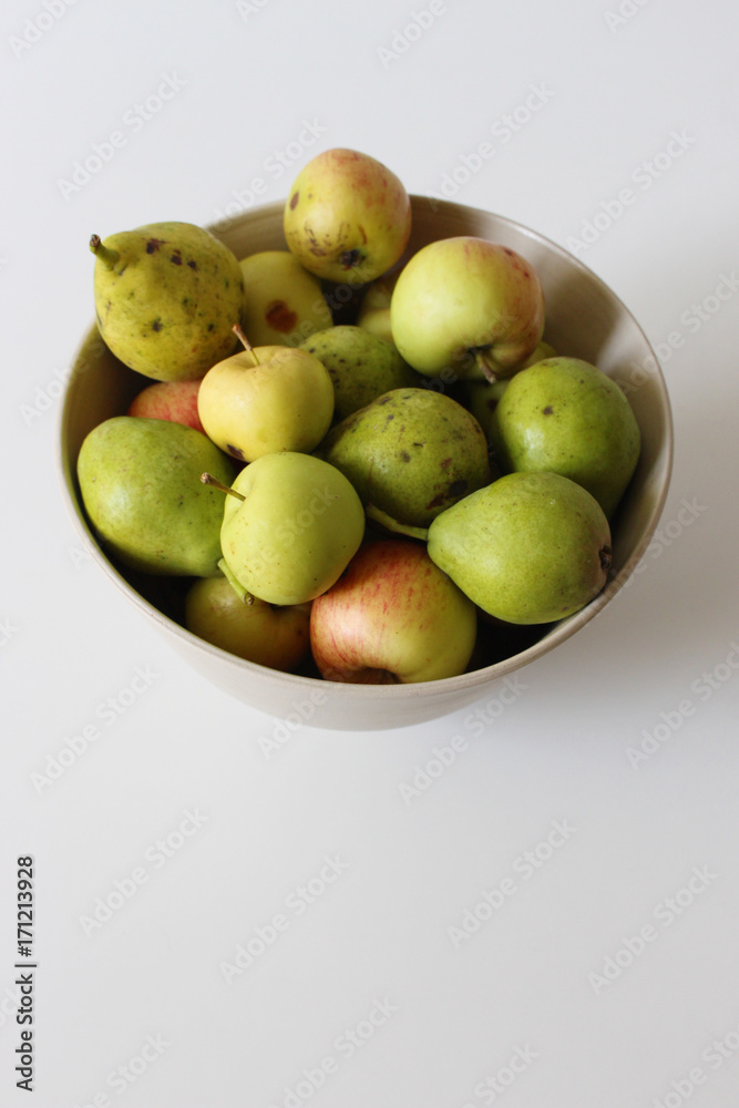 Apples and pears in bowl placed on white table Apples and pears in bowl placed on white table