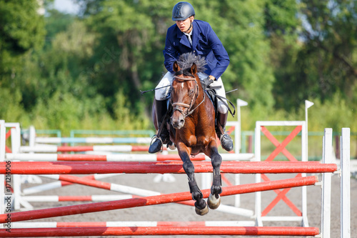 Young rider man on bay horse jumping over hurdle on show jumping competition © skumer