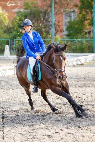 Young girl on bay horse galloping on her course on show jumping competition