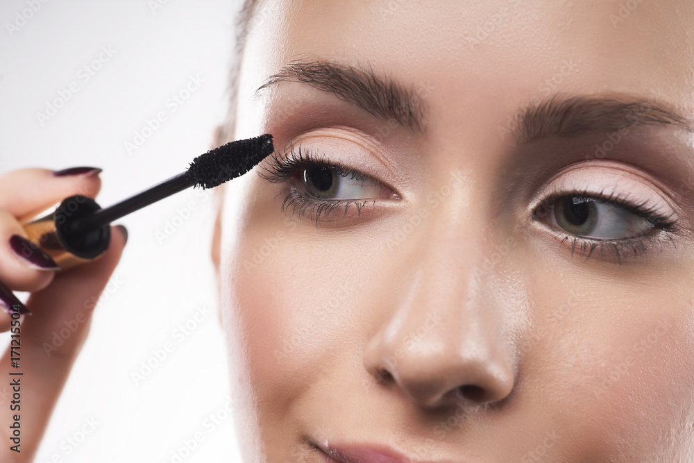Beautiful young girl with natural make-up puts mascara on eyelashes
