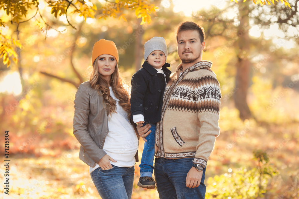 Fototapeta premium Young happy family have fun and walking in the autumn park. Pregnant woman with husband and little son