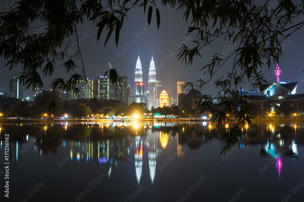 Night view of Kuala Lumpur skyline framed by bamboo tree leaves as seen from Taman Tasik Titiwangsa also known as Titiwangsa Lake Garden located in Kuala Lumpur, Malaysia.